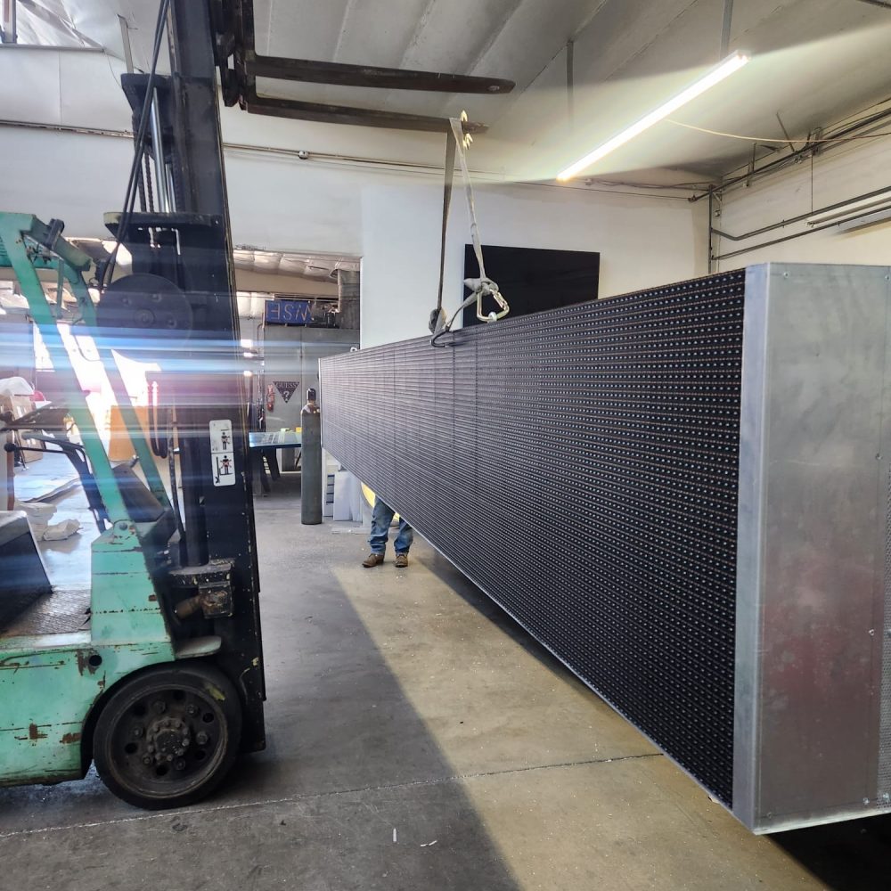 Large-format LED display cabinet being moved by forklift inside the Genius Signs fabrication shop