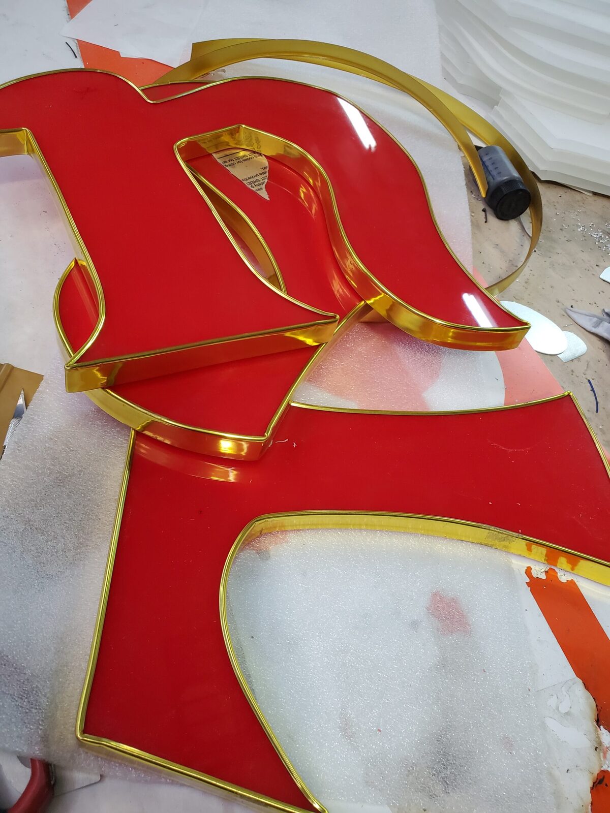 Red open-face channel letter with gold trim cap and exposed neon tube during fabrication
