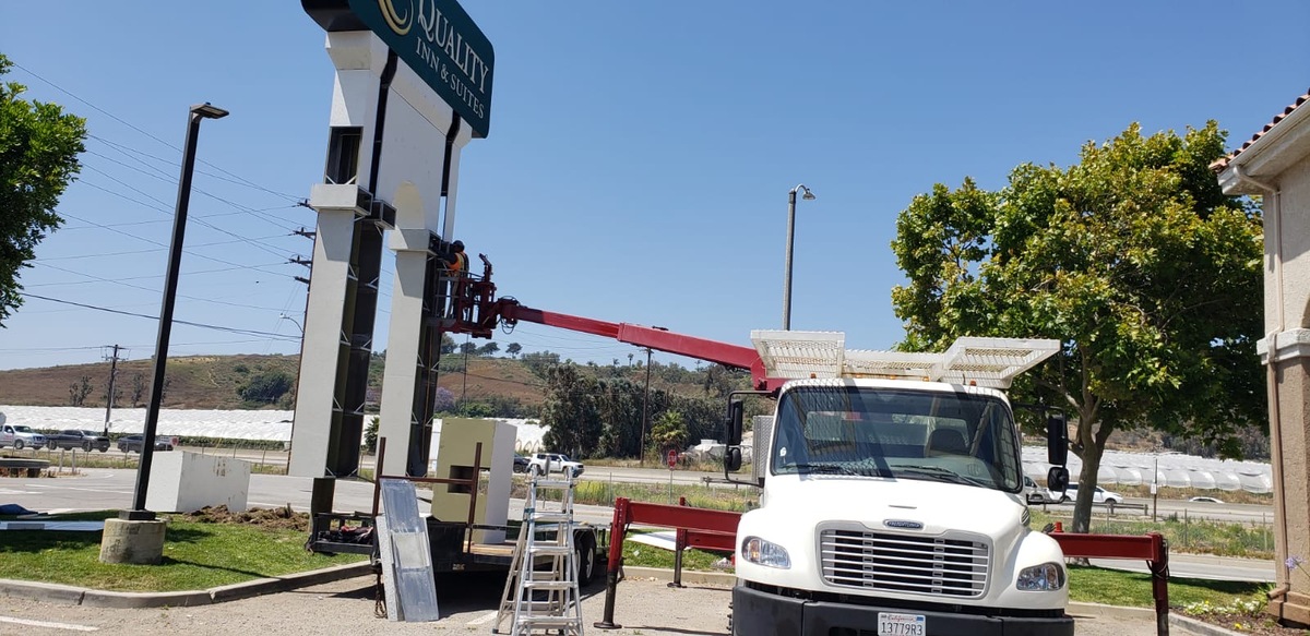 Crane truck setting the Quality Inn & Suites pylon structure, pole cover sections staged on the ground