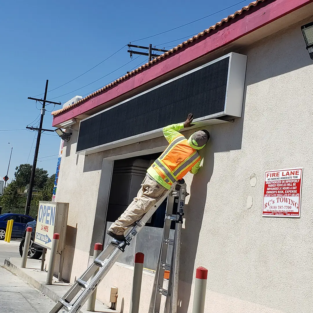 Technician installing an LED digital display panel on a commercial building
