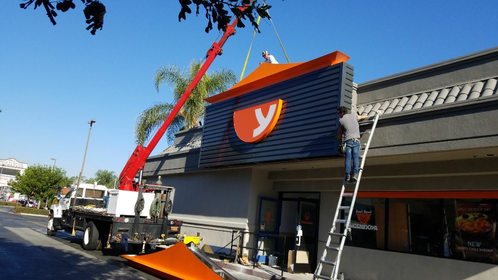 Crane installing cabinet sign on commercial building